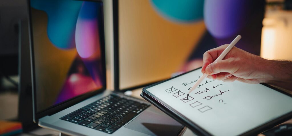 Digitalisierung in Fitnessstudios: Checkliste auf dem IPad vor zwei Bildschirmen und einem MacBook.